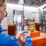 Besucherin fotografiert ein bunt verziertes Objekt mit einer Tischuhr (Hubertuslegende) 
© SKD, Foto: Carina Sonntag